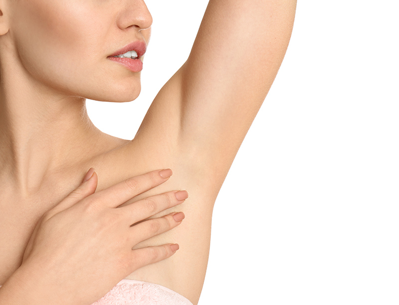 Close-up of a woman gently touching her smooth underarm with one hand while looking to the side, showcasing the results of hair removal or skincare treatment against a clean white background.